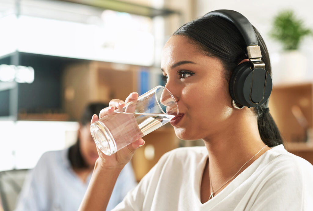 Shot of a young businesswoman drinking a glass of water at work.