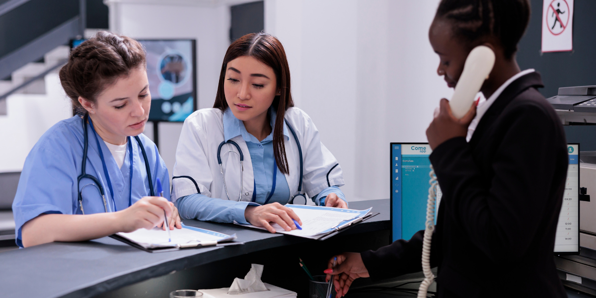 nurse and doctor at hospital desk talking, receptionist on phone
