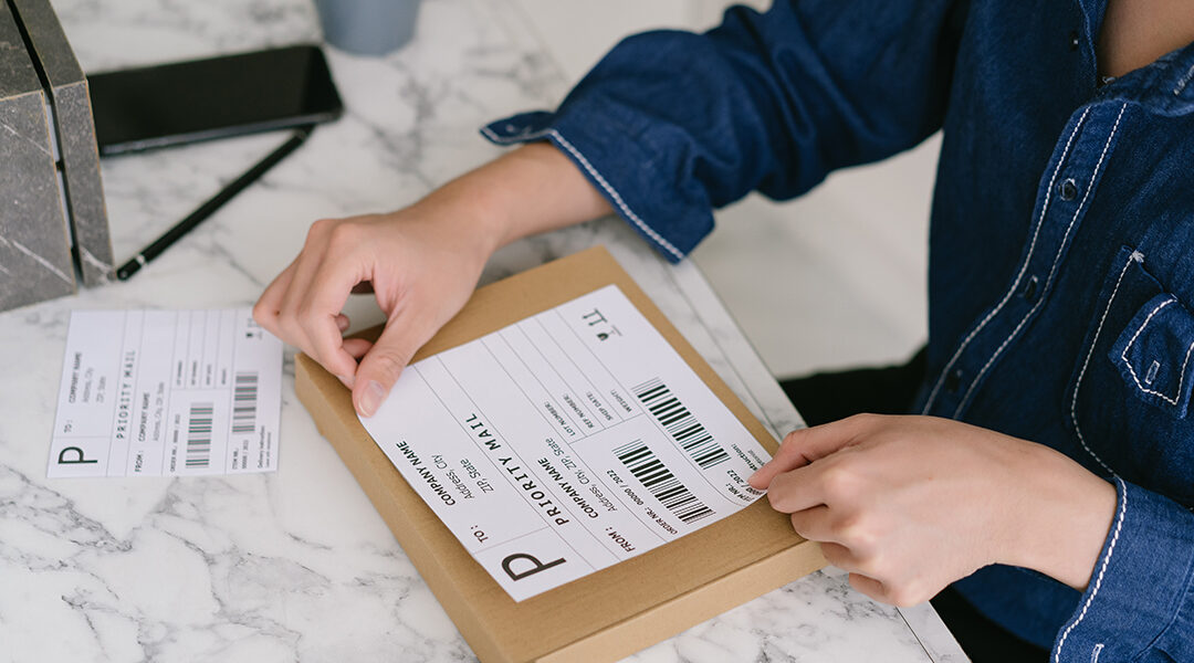 Person placing priority mail shipping label on small brown package