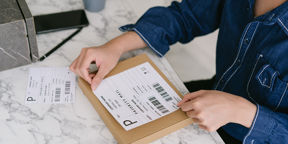 Person placing priority mail shipping label on small brown package